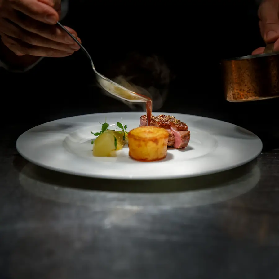 Chef finishing a plated dish with sauce